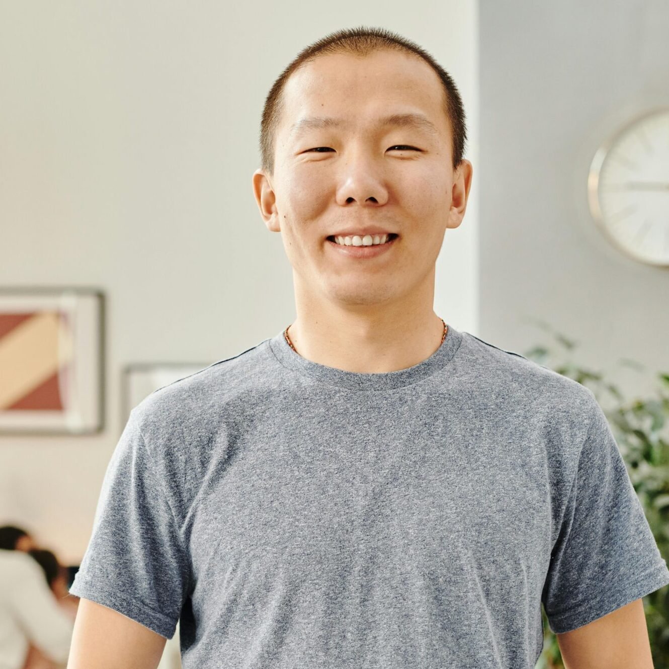 A cheerful man stands indoors, smiling with hands in pockets. Modern decor setting.