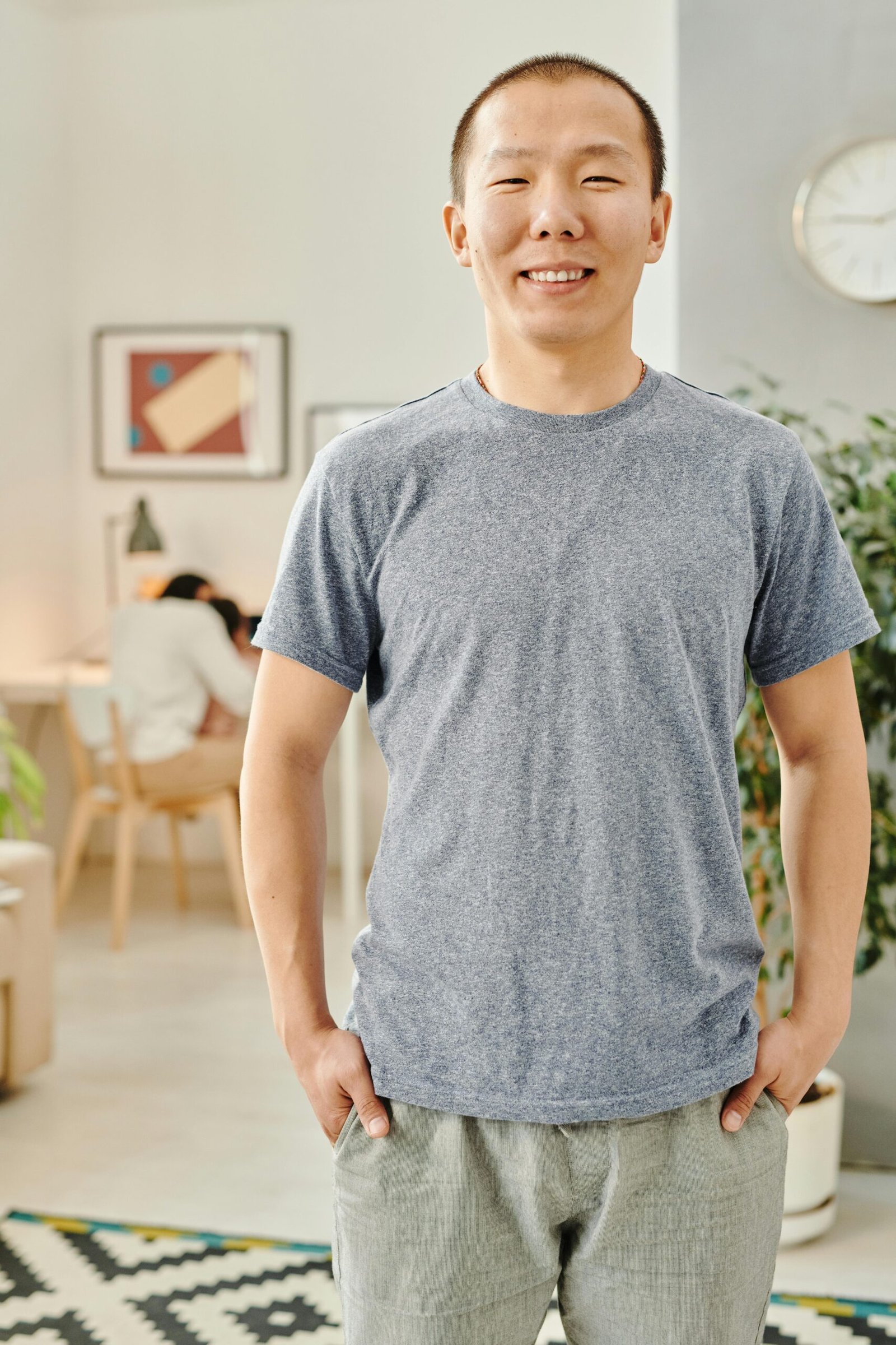 A cheerful man stands indoors, smiling with hands in pockets. Modern decor setting.