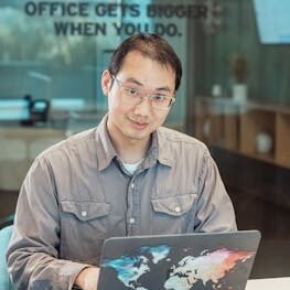 Asian man using colorful map laptop in a modern office setting