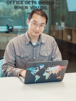 Asian man using colorful map laptop in a modern office setting